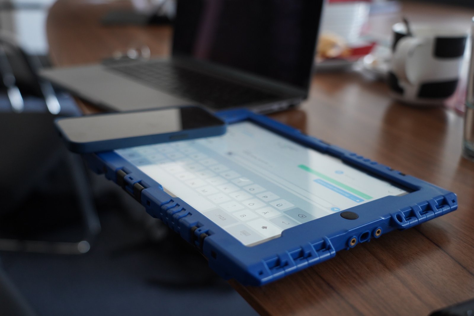 BJT05098 Ein Ipad in Schutzhülle zeigt die docYou med App. Es liegt auf einem Tisch neben Smartphone und Laptop