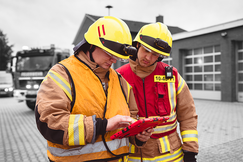 PulsationIT_50 min Zwei Mitarbeiter der Feuerwehr stehen vor einer Feuerwehrwache und bedienen docYou fire auf dem iPad