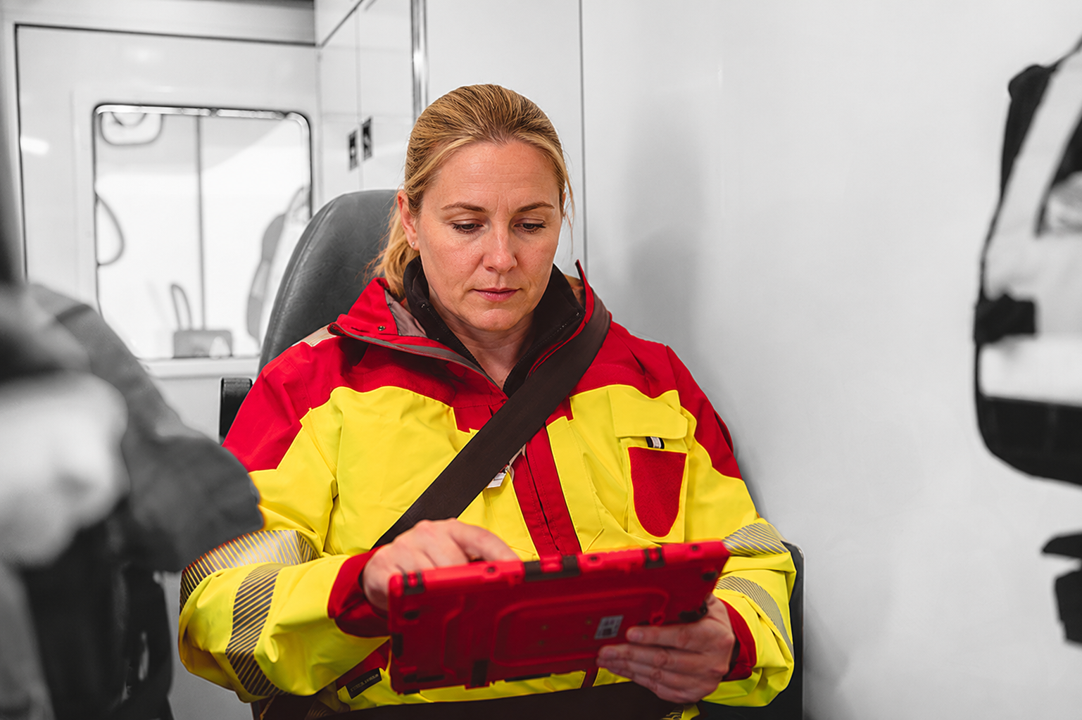 Mitarbeiterin des Rettungsdienstes sitzt angeschnallt in einem Rettungswagen und bedient docYou med auf einem iPad
